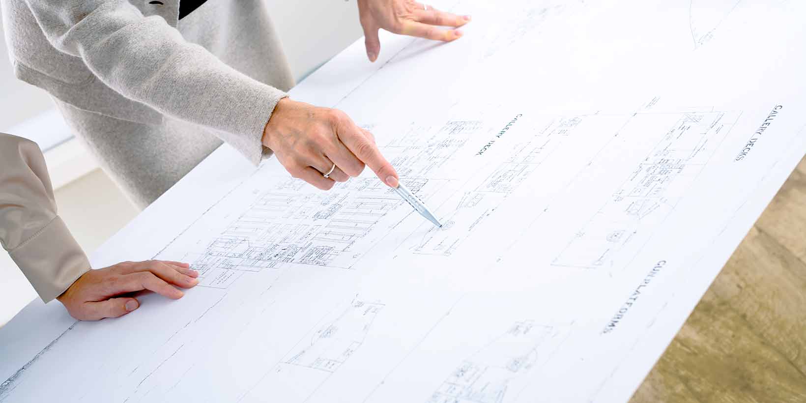 Frau in Business-Outfit zeigt auf ein Detail einer architektonischen Zeichnung.